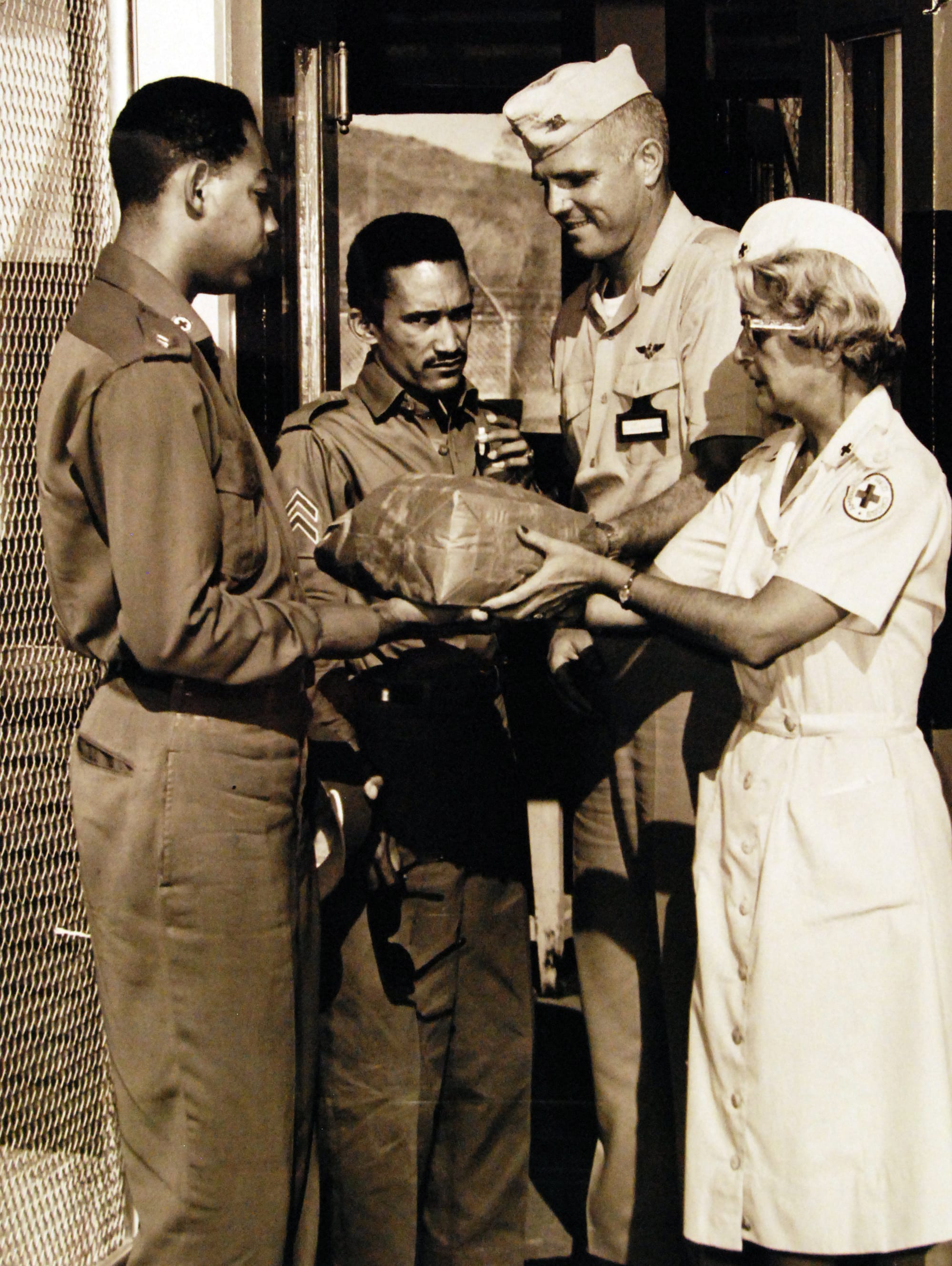 A soldier and nurse from the United States handing a package of polio vaccines to two Cuban soldiers.