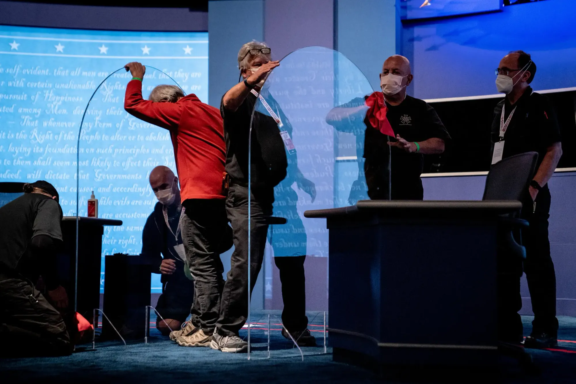 A group of stage hands wearing surgical masks erect plastic barriers between podiums on stage at the vice presidential debate in 2020.